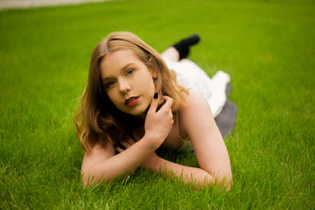 A teenager girl lies on the grass in a beautiful white dress, rests, enjoys nature. Girl with short blond hair. Beautiful and healthy skin and youth smileの写真素材
