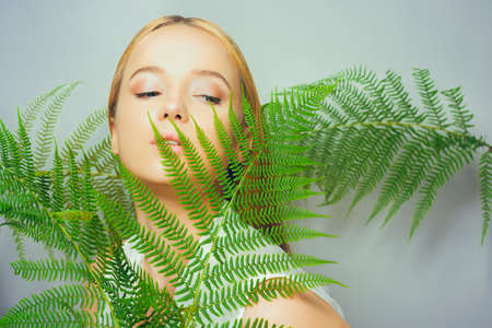 Beautiful young blond woman with perfect skin and natural make up posing front of plant tropical green leaves background. Teen model hair care of her face Fashion.の写真素材