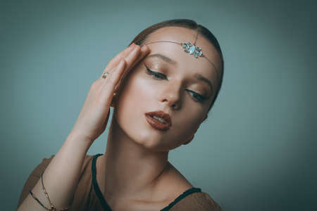 Girl with Dubai make-up. Perfect arrows, red lips, gold jewelry, jewelry on the forehead. Indian girl, indian jewelry.の写真素材
