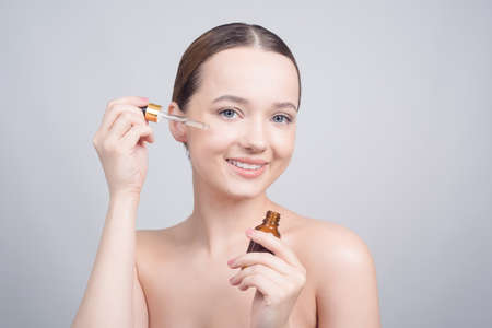 Close up of pretty brunette lady applying cosmetic oil on her face with pipette. Beauty therapy concept. Clean skin and face care. Youth and cosmeticsの写真素材