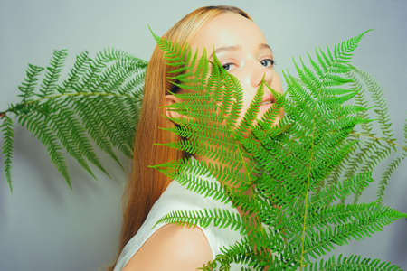 Beautiful young blond woman with perfect skin and natural make up posing front of plant tropical green leaves background. Teen model hair care of her face Fashion.の写真素材
