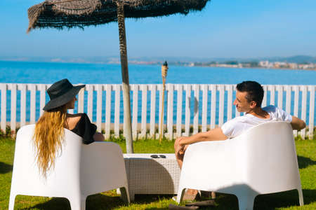 Lovers sitting, looking into sky and sea, mountion, under sun umbrella. Vacation, tourism, hooneymoon. Girl with a long hair.の写真素材