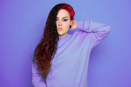 Woman in a blue sweater on a blue background posing. A beautiful brunette with long hair and and tunnels in her ears. Eyeliner and trendy makeupの写真素材