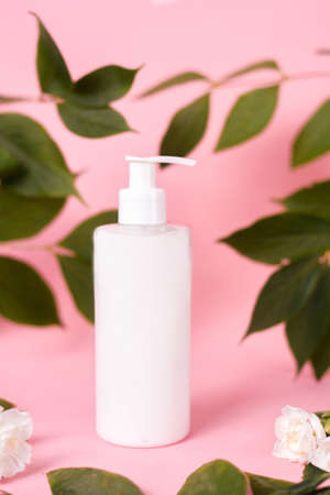 Cosmetics, cream with dispenser, lotion on a pink background. White bottle on a background of leaves and flowers. Natural cosmeticの写真素材