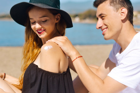 Suncare couple on a summer beach vacation have good skincare with high spf sunblock. Couple applying suncream. Handsome man putting sun tan lotion on his girlfriend at the beach.の写真素材