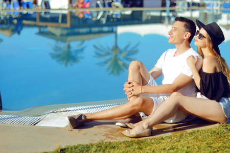 A sunny day, a man and a girl enjoy the rest. Travel. Against the background of palm trees and houses. Couple at the hotel with a pool. The concept of relaxation and travel. Kissの写真素材