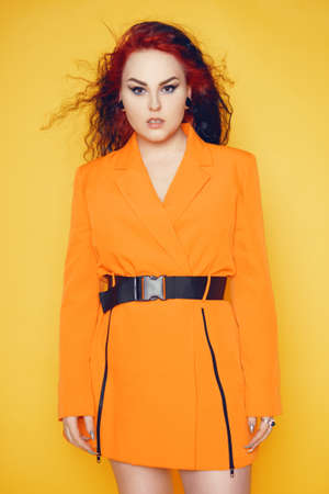A woman with red roots and black hair. Unusual hairstyle, hairdresser, wind in your hair. Girl on a yellow background in an orange dress. Fashion and beauty.の写真素材