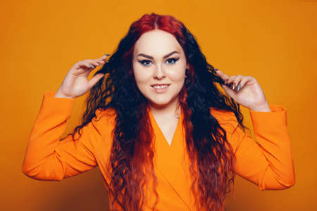 A woman with red roots and black hair. Unusual hairstyle, hairdresser, wind in your hair. Girl on a yellow background in an orange dress. Fashion and beauty.の写真素材