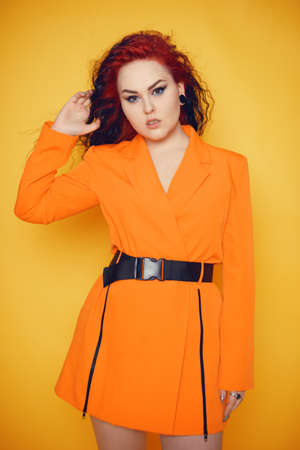 A woman with red roots and black hair. Unusual hairstyle, hairdresser, wind in your hair. Girl on a yellow background in an orange dress. Fashion and beauty.の写真素材