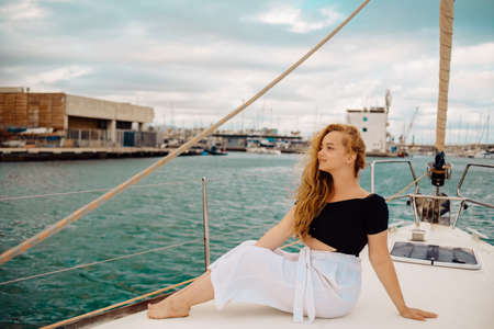 A beautiful long-haired girl sits on the bow of a barred yacht and enjoys life. The blonde is resting in the open sea or ocean.の写真素材