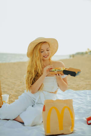 A posh girl eats food from a delivery service on the beach from a nearby restaurant. Model eats...