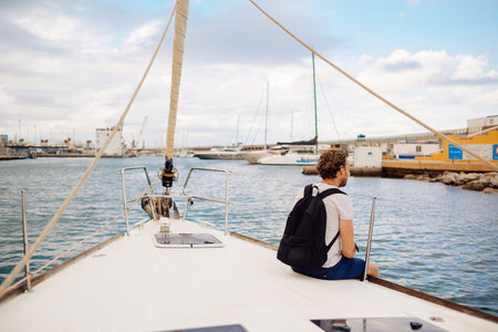 Guy traveler with a backpack sits on a sailing yacht and enjoys the views. A man on a yacht in the ocean, summer dayの写真素材