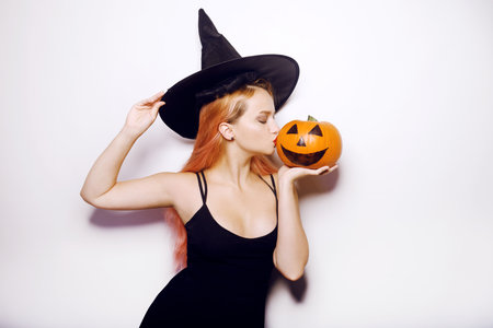Beautiful girl witch is holding a pumpkin in her hands. Woman celebrates halloween, joy and a smile on her face. Model kissing pumpkin.の写真素材