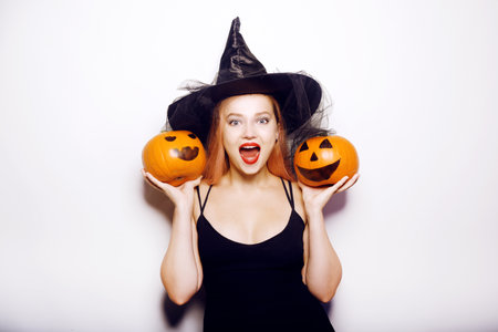 Beautiful girl witch is holding a pumpkin in her hands. Woman celebrating halloween, joy and a smile on her face.の写真素材