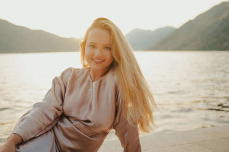 Portrait of a beautiful young smile blonde against a background of mountains and the sea, beautiful nature. Travel at sunsetの写真素材
