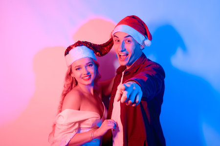 New Year's party, a girl and a guy in a Santa hat are smiling and dancing. Beautiful couple in christmas in neon.の写真素材
