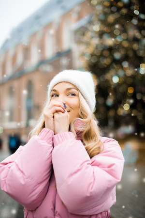 Cute portrait of a girl in the winter on the street, the snow is falling, the blonde on the...