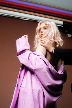 A blonde woman in a pink jacket, a jacket in sequins poses in the studio on a brown background. High fashion, 90s 80s. The girl dances and moves. Model with pink makeupの写真素材