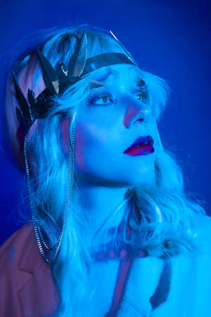 Queen in a silver crown, trendy stylish neon photo. The woman is all in jewelry and bijouterie. Red blue light. Evening make-up, red lips and shadows in sparkles.の写真素材