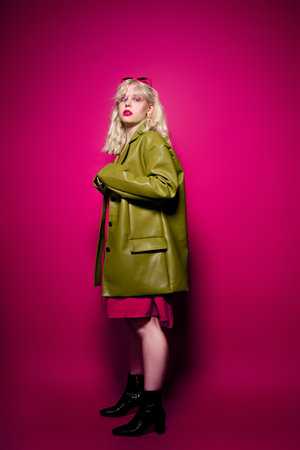 Girl in a stylish green coat on a pink background. Blonde with short hair make up in sparkles. Style and fashion, grunge styleの写真素材