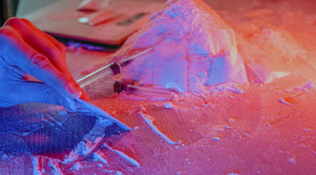 Drugs, drug dealer house. Cocaine packaged in sachets, scales: tablets and syringes in neon light. Illegal, entry.の写真素材