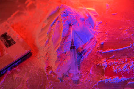 Drugs, drug dealer house. Cocaine packaged in sachets, scales: tablets and syringes in neon light. Illegal, entry.の写真素材