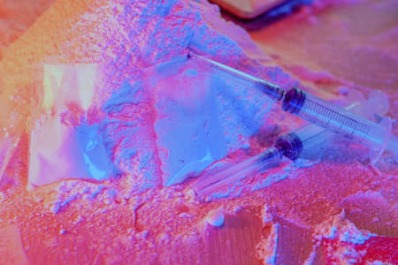 Drugs, drug dealer house. Cocaine packaged in sachets, scales: tablets and syringes in neon light. Illegal, entry.の写真素材