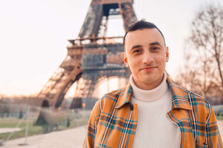 Guy tourist on the background of the Eiffel Tower posing. Male tourist laughs and smiles. Handsome brunette on a trip.の写真素材