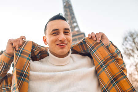 Guy tourist on the background of the Eiffel Tower posing. Male tourist laughs and smiles. Handsome brunette on a trip.の写真素材