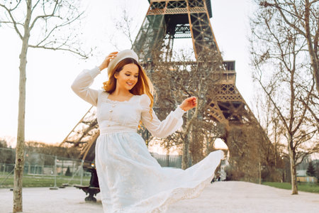 Beautiful blonde in Paris with the Eiffel Tower in the background in a beret and white dress. The woman is laughing and smiling, the girl is on a trip to France.の写真素材