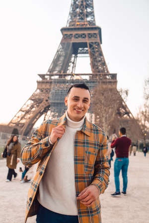 Guy tourist on the background of the Eiffel Tower posing. Male tourist laughs and smiles. Handsome brunette on a trip.の写真素材