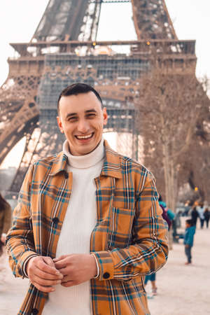 Guy tourist on the background of the Eiffel Tower posing. Male tourist laughs and smiles. Handsome brunette on a trip.の写真素材
