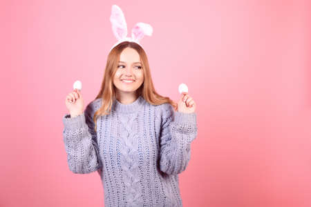 Beautiful girl in a blue sweater on a pink background. Woman with bunny ears, posing for easter, girl smiling, space for text.の写真素材