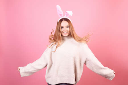 A girl with rabbit ears dances on a pink background. Easter holiday, smile and party. The girl is posing in the studioの写真素材