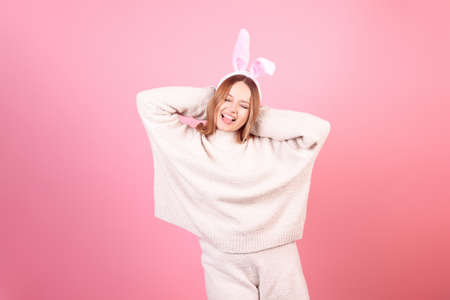 A girl with rabbit ears dances on a pink background. Easter holiday, smile and party. The girl is posing in the studioの写真素材