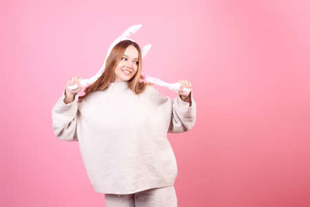 Beautiful girl in rabbit ears on a pink background laugh, Easter holidays. The woman smiles. Looks to the side, space for text, funの写真素材