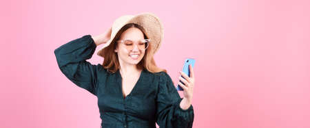 A girl in a straw hat and sunglasses speaks on the phone on a pink background. Tourist traveler in...