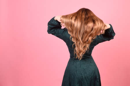Girl on a pink background with gorgeous long hair, hair care. Brunette, redhead model with curled hair.の写真素材