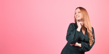 A beautiful brunette girl with long hair on a pink background in a green dress looks to the side, a lot of space for text.の写真素材
