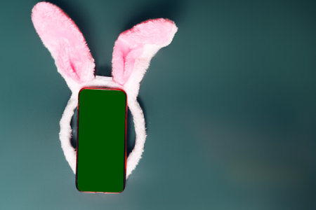 Phone on green background, greenscreen place for mocap. Easter bunny or rabbit ears on the phone, space for text.の写真素材