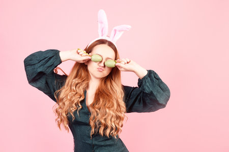 Easter girl closes her eyes with Easter eggs on a pink background.の写真素材