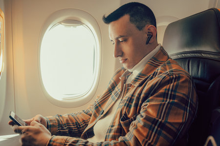 A man sits in an airplane at the window and looks into a smartphone.の写真素材
