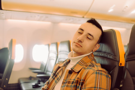 A man in a half-empty plane sleeps. Calm travel in an airplane, tablet for calming, sleepingの写真素材