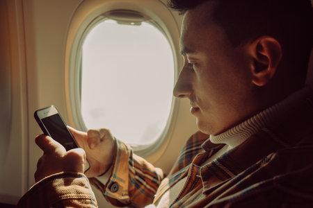A man in a half-empty plane with a phone. Guy traveler looking at smartphoneの写真素材