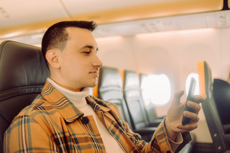 A man in a half-empty plane with a phone. Guy traveler looking at smartphoneの写真素材