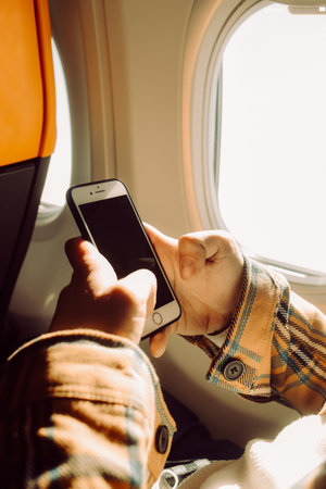 Male hands holding a smartphone in an airplane near the portholeの写真素材