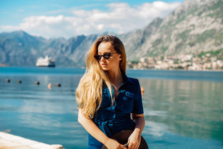 A woman in sun glasses and a hat stands against the backdrop of the sea and mountains. Vacation and outdoor recreation. Girl with long hair on vacationの写真素材