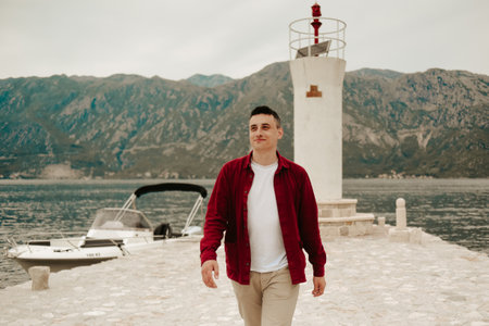 A man in a white T-shirt and red shirt walks on the island near the lighthouse. Travel, Montenegro.の写真素材