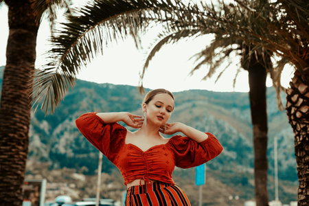 Stylish woman in summer on the background of palm trees and mountains. Spanish girl in a red suit and long earringsの写真素材