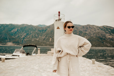 A stylish girl in a warm white suit walks on the island near the lighthouse. Travel, Montenegro.の写真素材